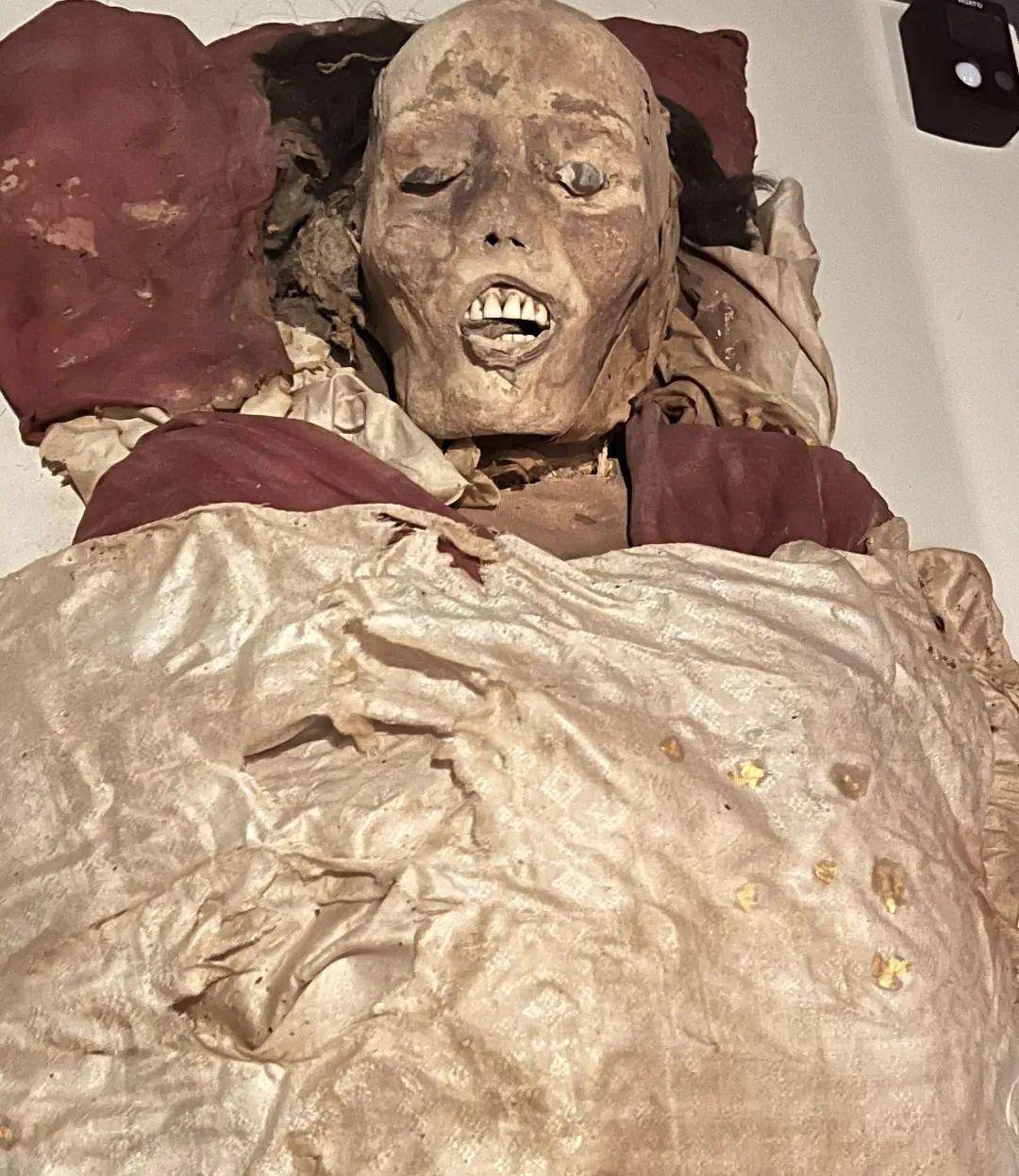 女尸身穿两层衣物,贴身为红色交领高腰连身绢裙,外套白色圆领长袍