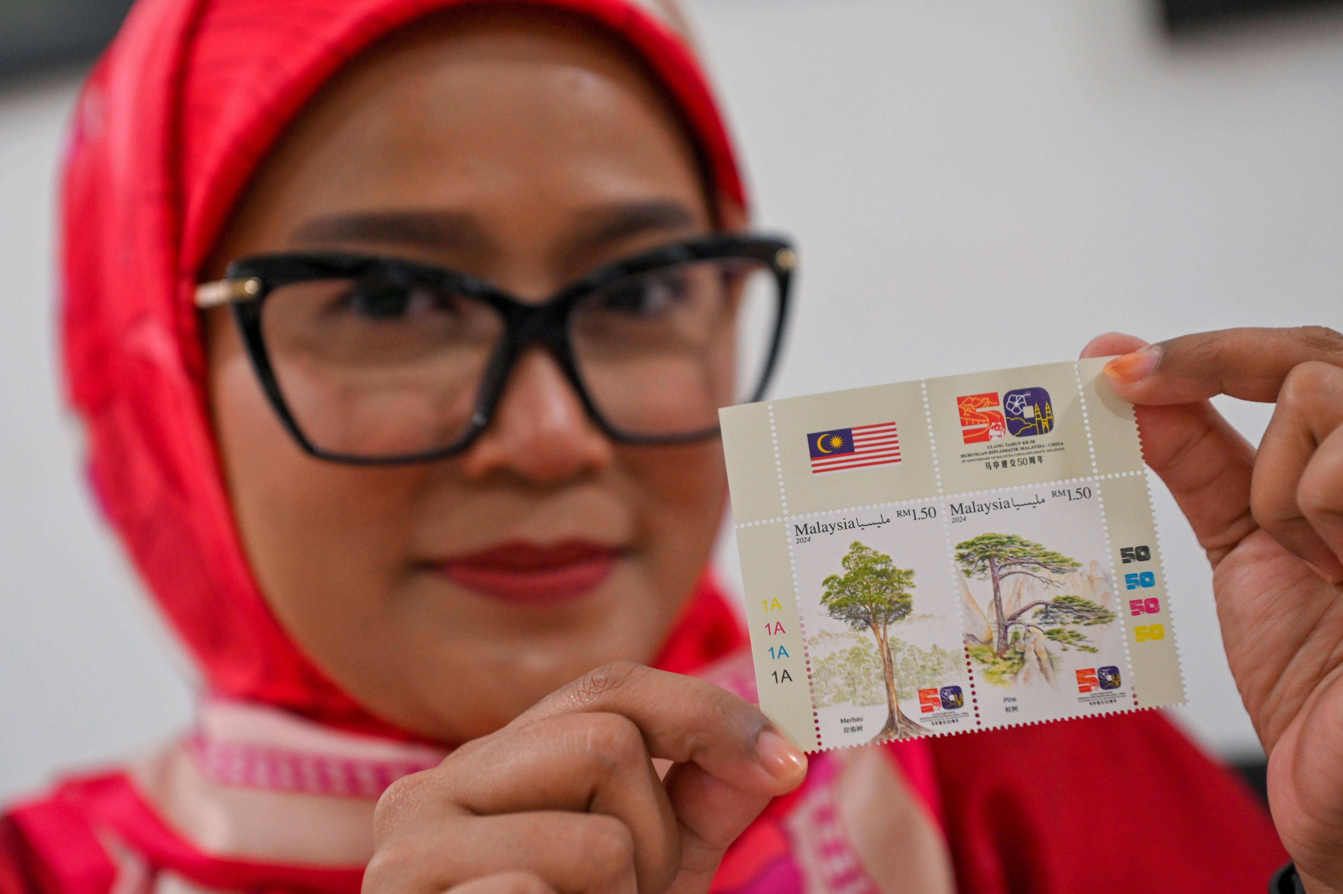 马来西亚吉隆坡,顾客展示购买到的《中马建交五十周年》联合纪念邮票